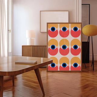 Print leaning on a floor showing Wall Art Eye with abstract eyes in muted orange and coral beside a yellow lamp