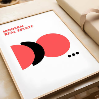 Framed close-up of Red Black and White wall art with modern real estate text and abstract shapes on a table