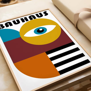 Framed print close-up of retro wall art with stylized eye in teal, ochre and black leaning on a wooden surface