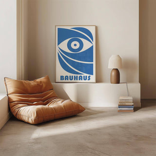 Print leaning on a shelf showing stylised blue eye and Bauhaus text next to a brown leather chair