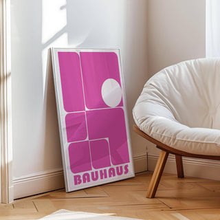 Print leaning on a floor with pink geometric shapes and a white circle near a white cushioned chair
