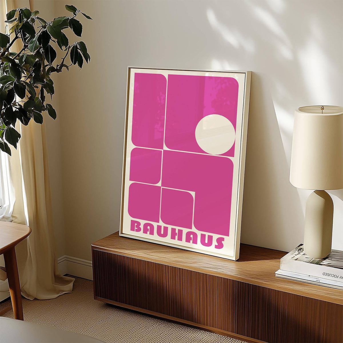 Wall Art Pink print leaning on a wooden sideboard with a lamp and plant nearby in a softly sunlit room