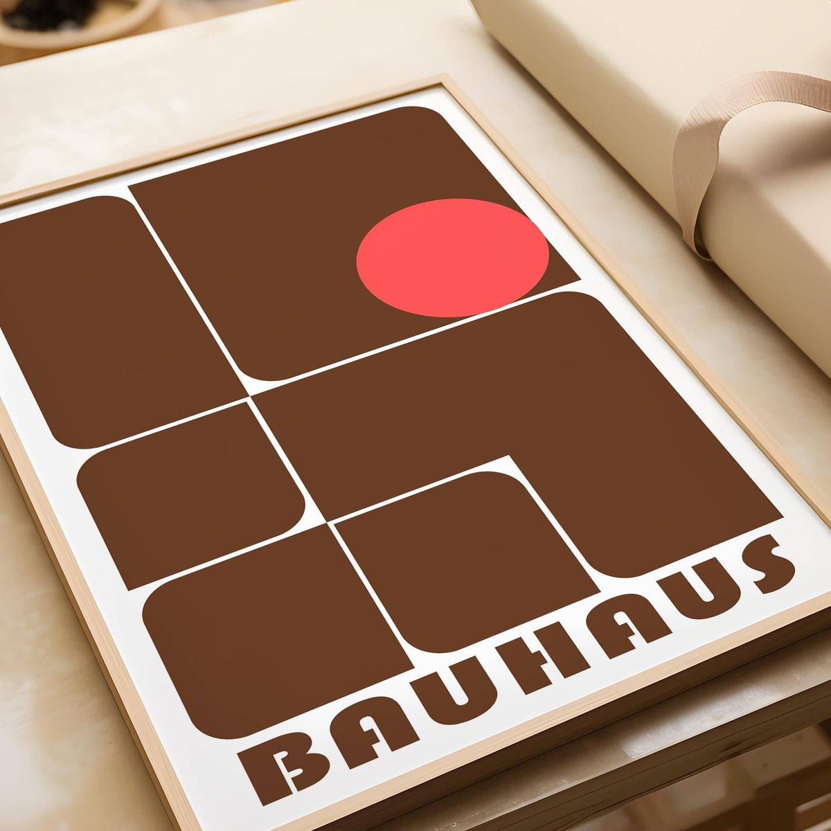 Close-up of wall art with brown geometric shapes and a red circle leaning on a wooden surface next to wrapping paper