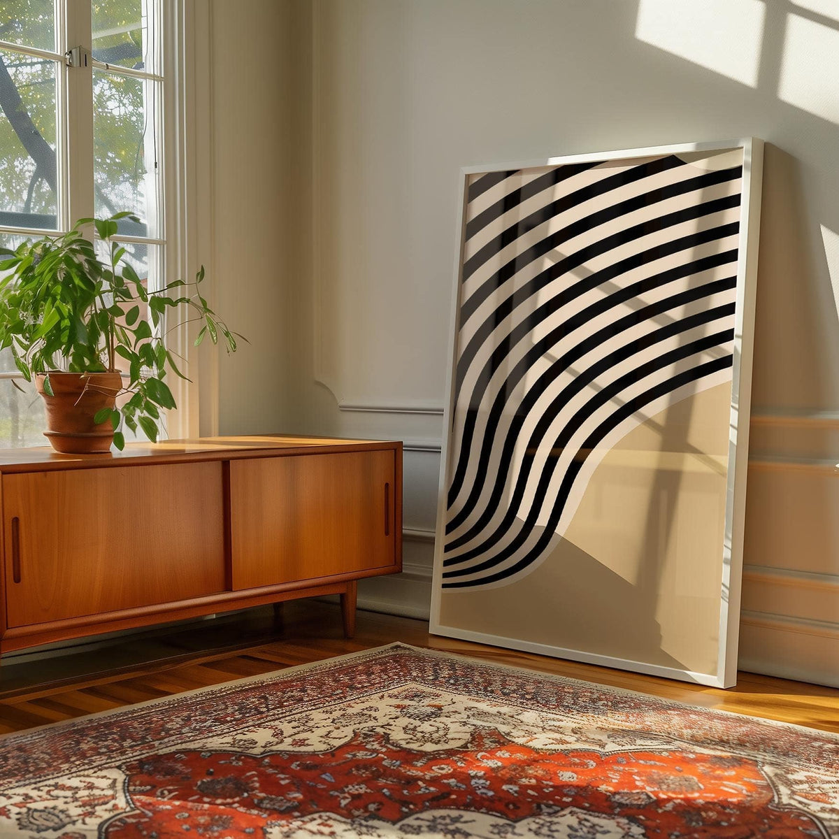 Print leaning on floor with beige abstract art featuring black curved stripes beside a wooden sideboard and plant