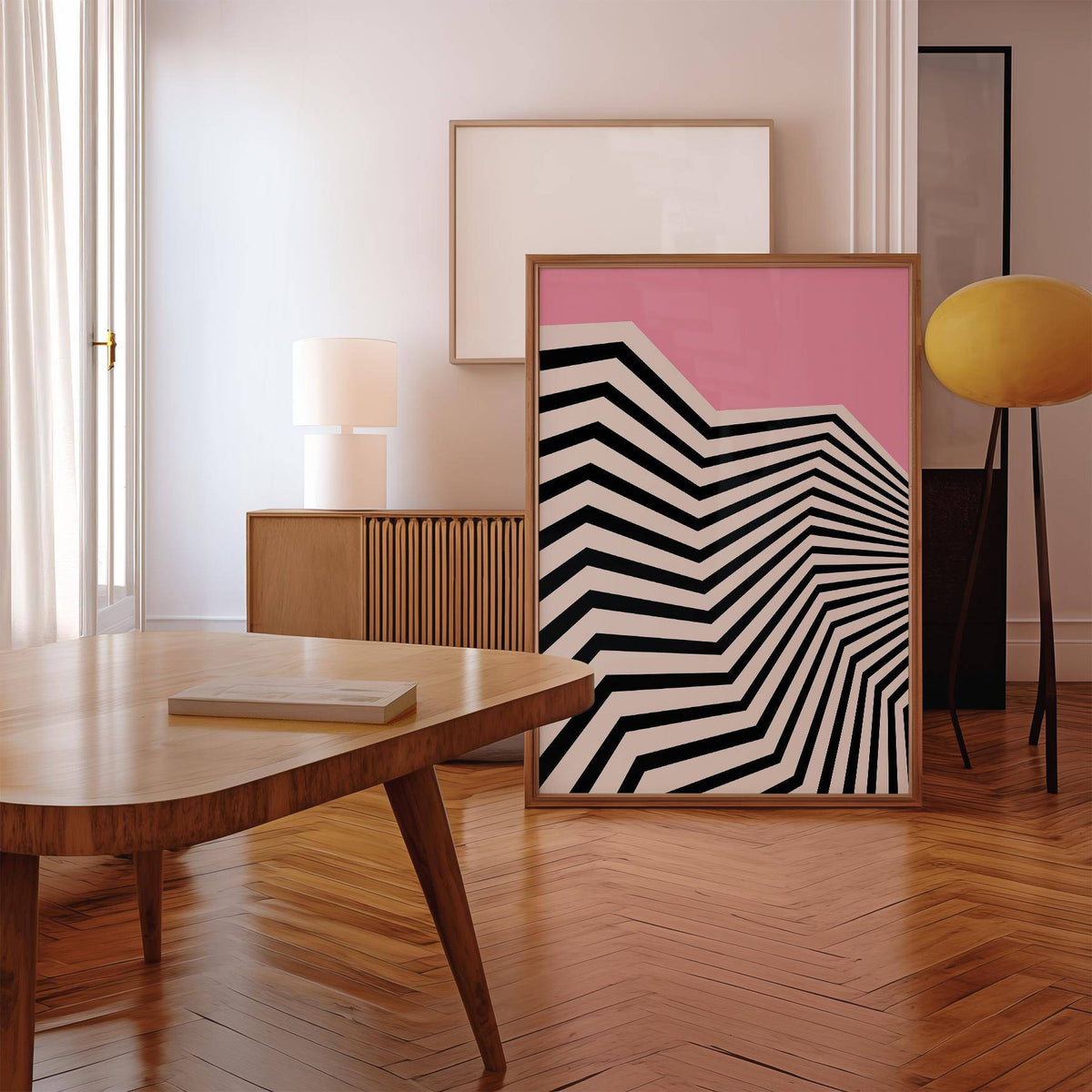 Wavy wall art with black and white zigzag pattern and pink background leaning on a floor in a room with wooden flooring and table