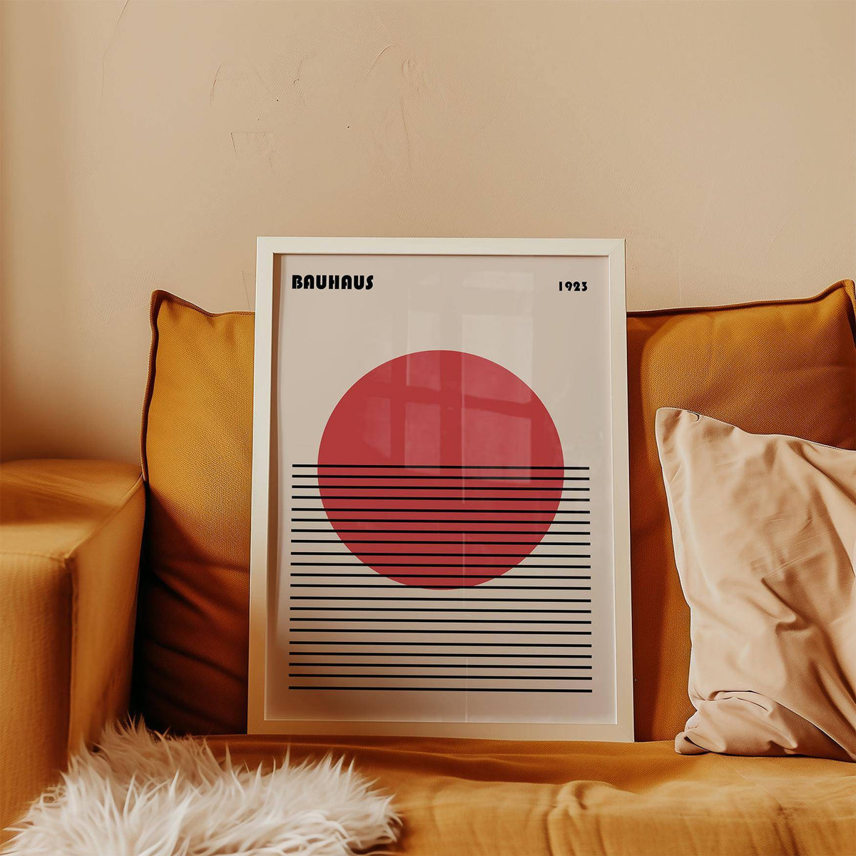 Framed Geometric Art Print with a red circle and black lines leaning on an orange sofa with cushions