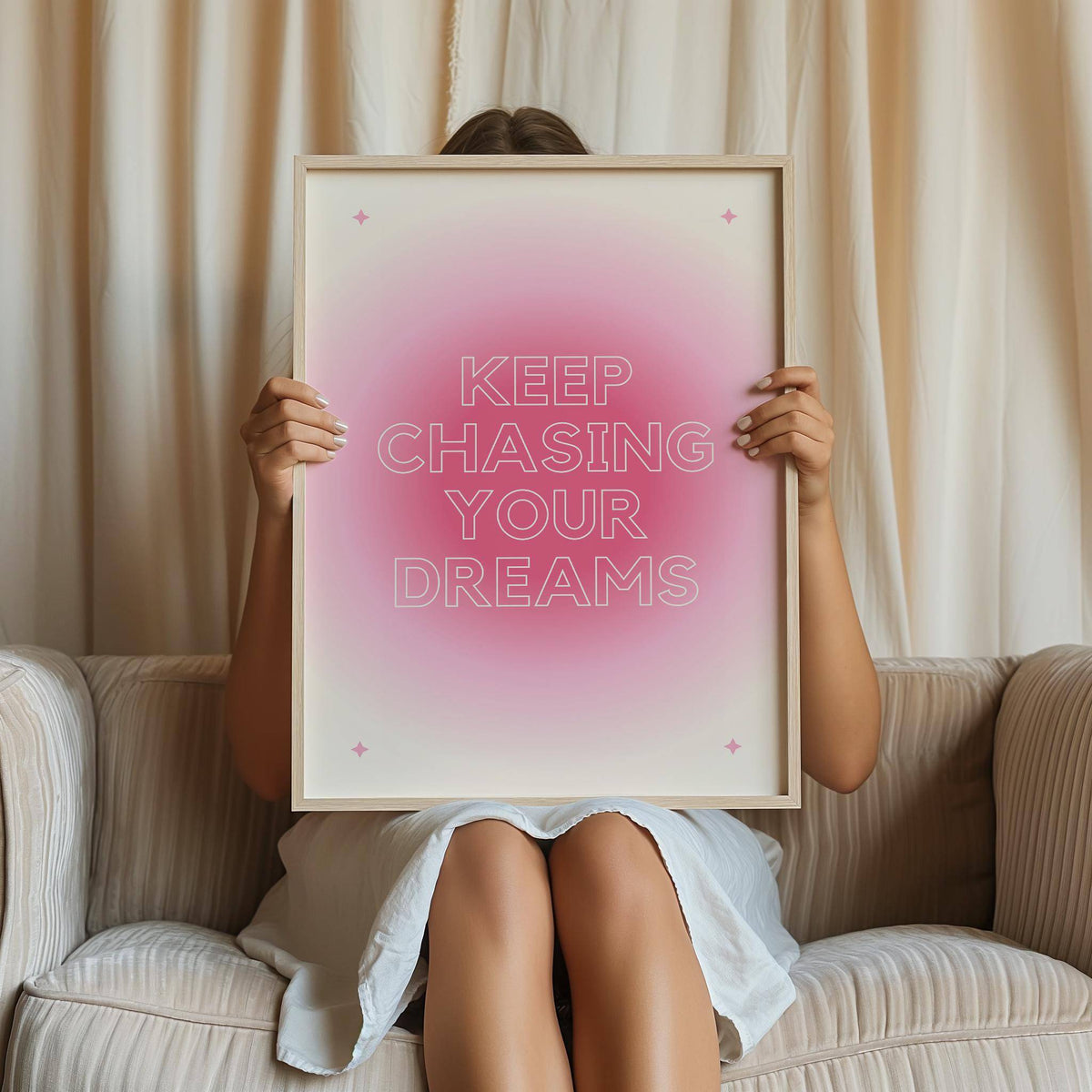 Framed print of motivational text with pink gradient and stars held by a seated person on a sofa