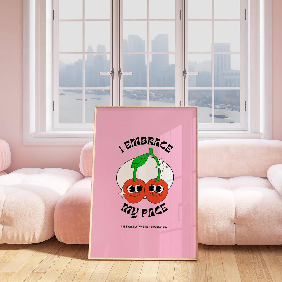 Print leaning on a pink sofa of a pair of cherries with green stems on a pink background