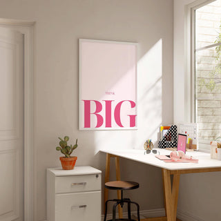 Print on a wall of think big typography in pink and white with a cactus on a drawer nearby in a bright study room