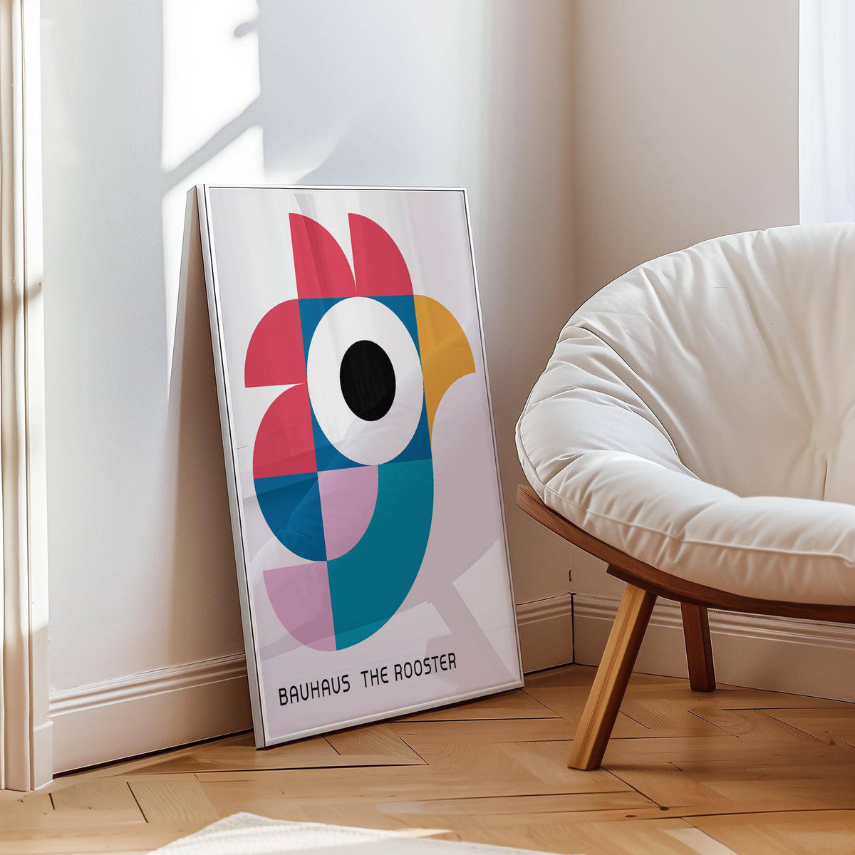 Print leaning on floor showing geometric pattern art of an abstract rooster in pink and blue beside a white cushioned chair