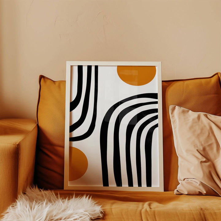 Framed orange and black wall art with curved arcs and circles resting on a brown sofa with cushions