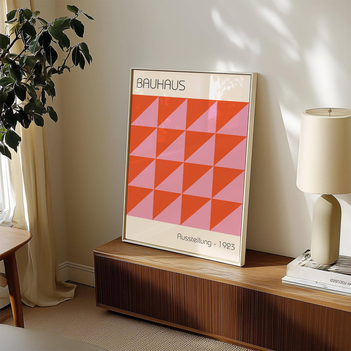 Modern Wall Art print leaning on a wooden sideboard next to a lamp and plant in natural light
