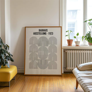 Print leaning on wooden floor with Bauhaus Minimalism Art of black line arches and text near plants and leather chair
