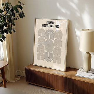 Print leaning on a cabinet of Bauhaus Minimalism Art with black line arches beside a lamp and books