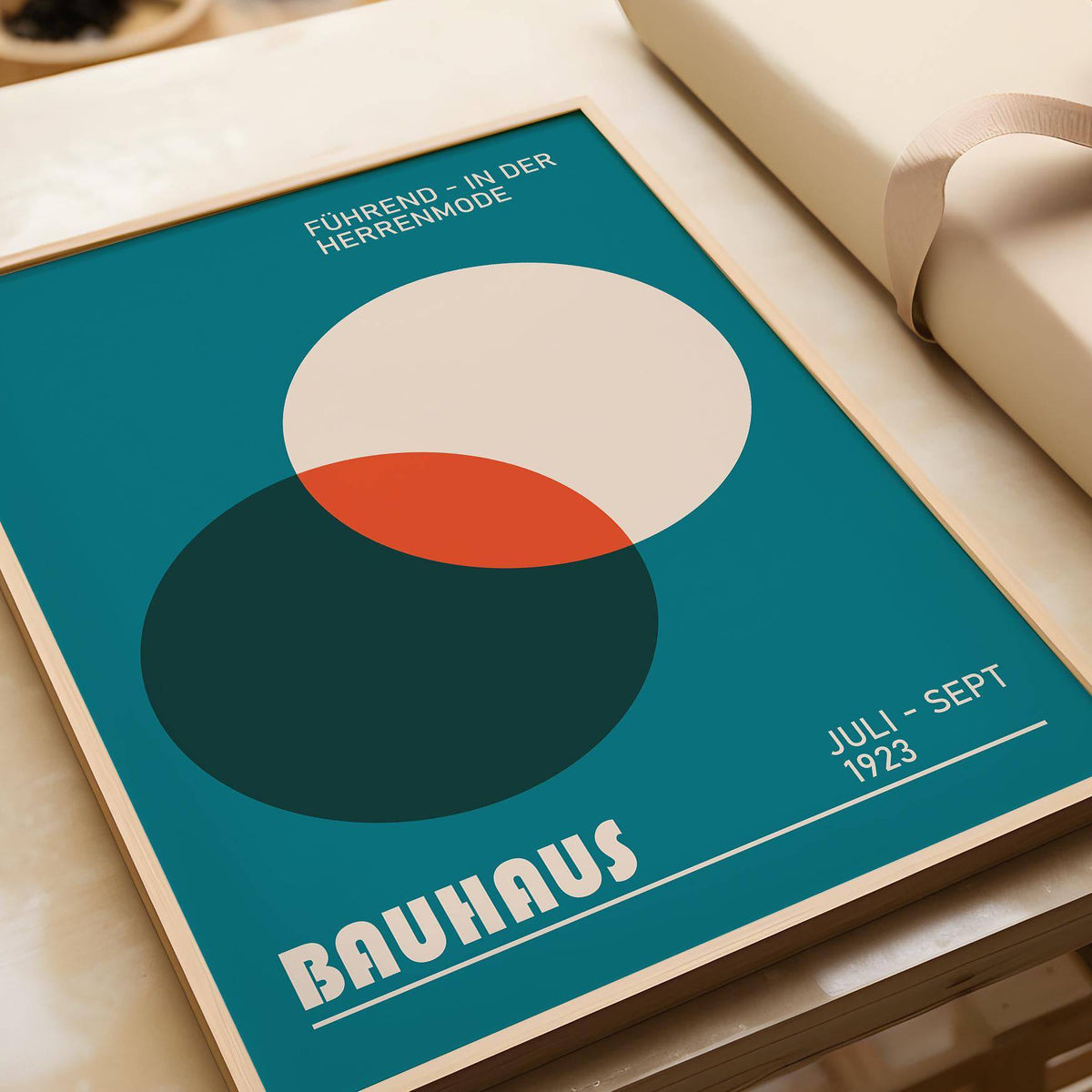Framed close-up of Modern Office Wall Art with overlapping circles in teal, cream, and rust on a table with wrapping paper