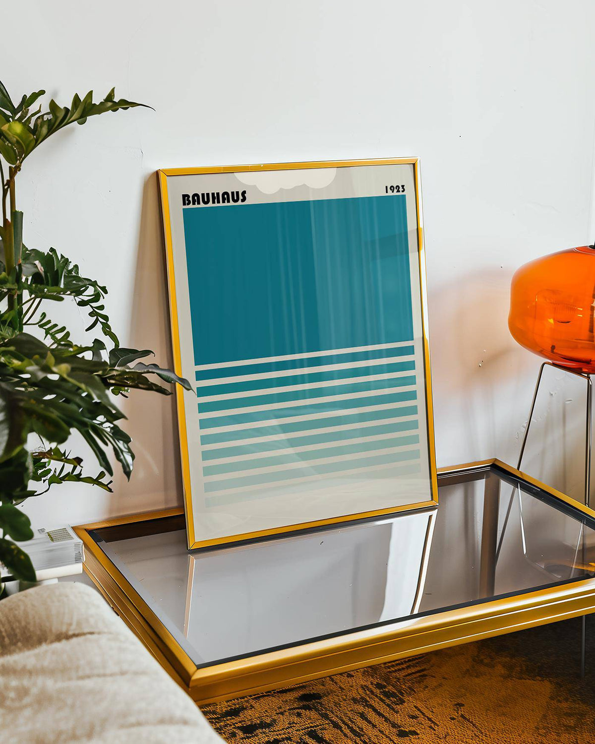 Teal Blue Gradient wall art leaning on a glass table with gold frame beside an orange chair and green plant