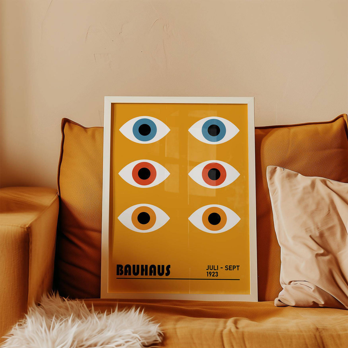 Eye Poster leaning on a mustard sofa with stylised Bauhaus eyes in blue orange and black