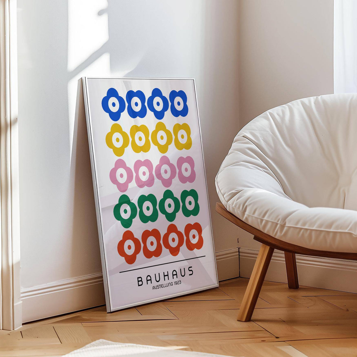 Print leaning on a floor showing colourful stylised flowers with bauhaus typography beside a white cushioned chair