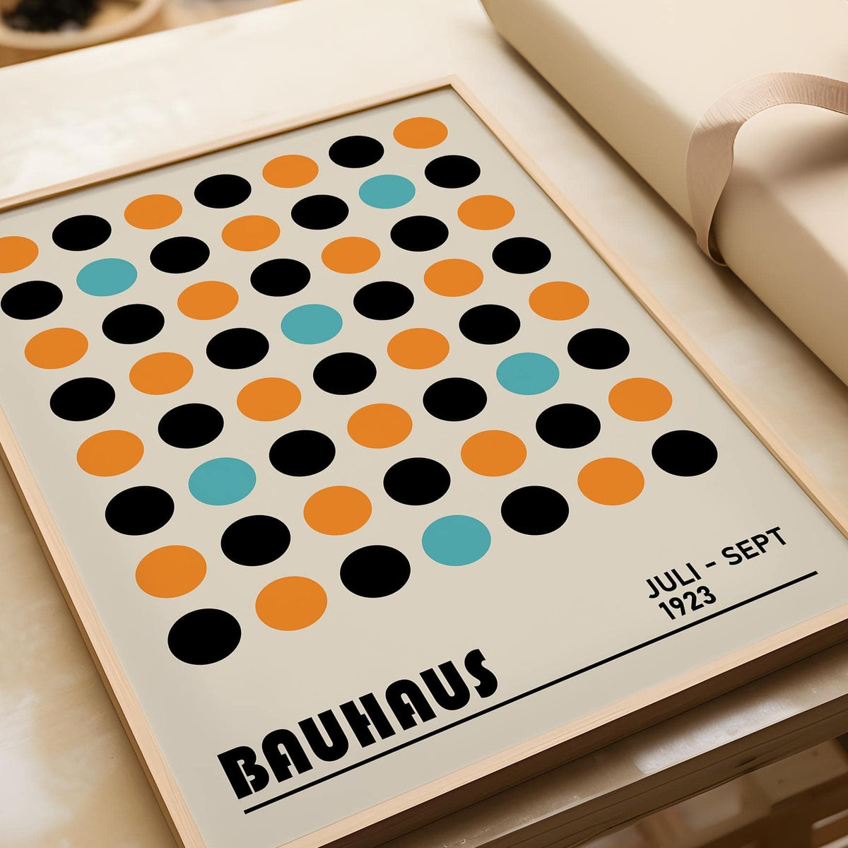 Framed close-up of geometric wall decor with multicolour dots and bauhaus text leaning on a cream surface