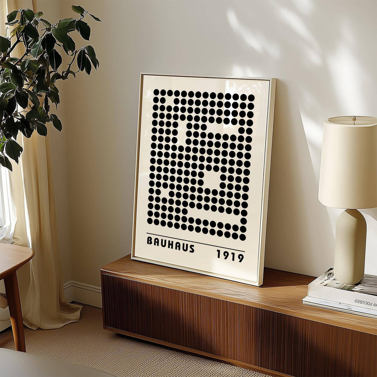 Print leaning on a wooden sideboard black dots pattern with Bauhaus text beige wall and lamp nearby