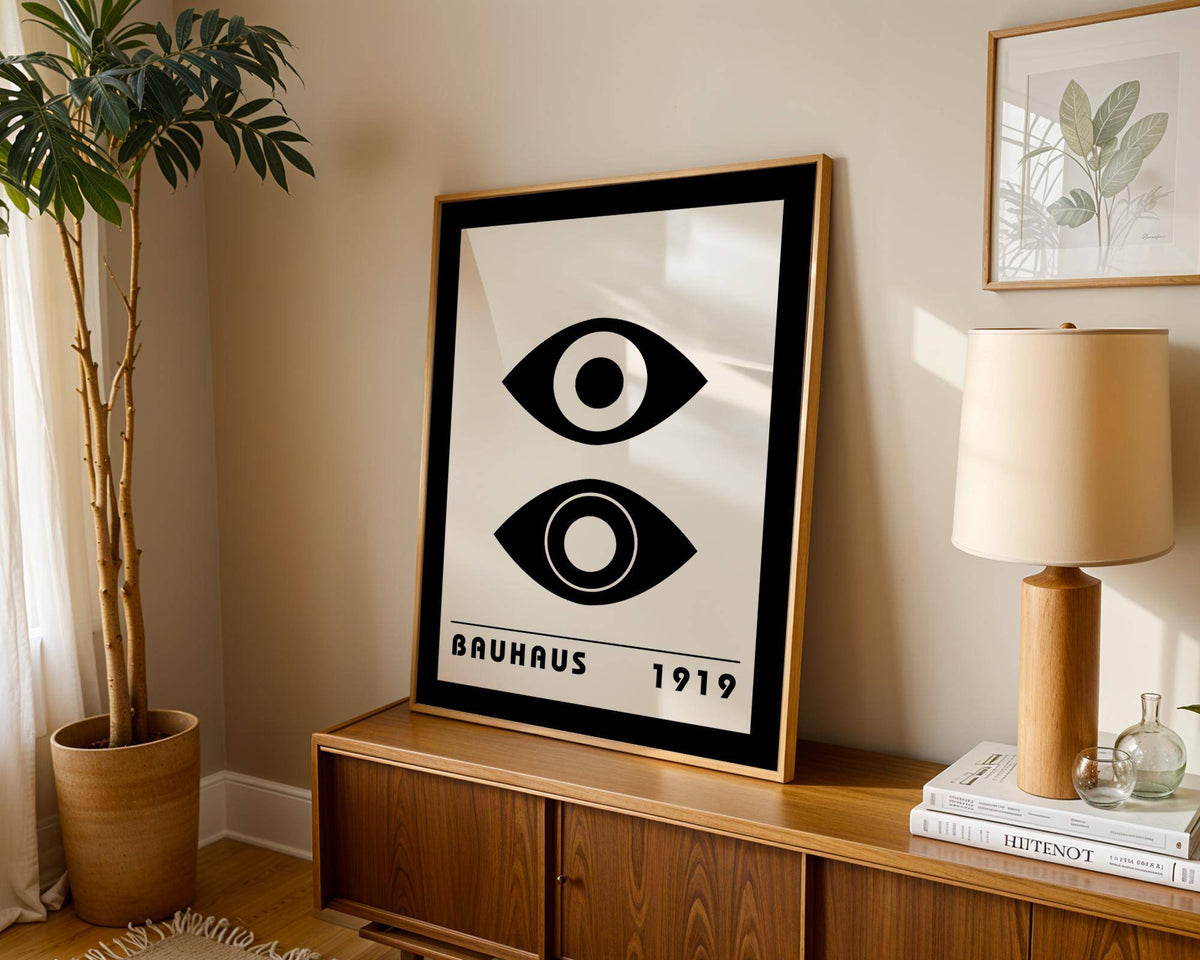 Bauhaus art print of stylised black and white eyes leaning on a wooden sideboard with a lamp nearby