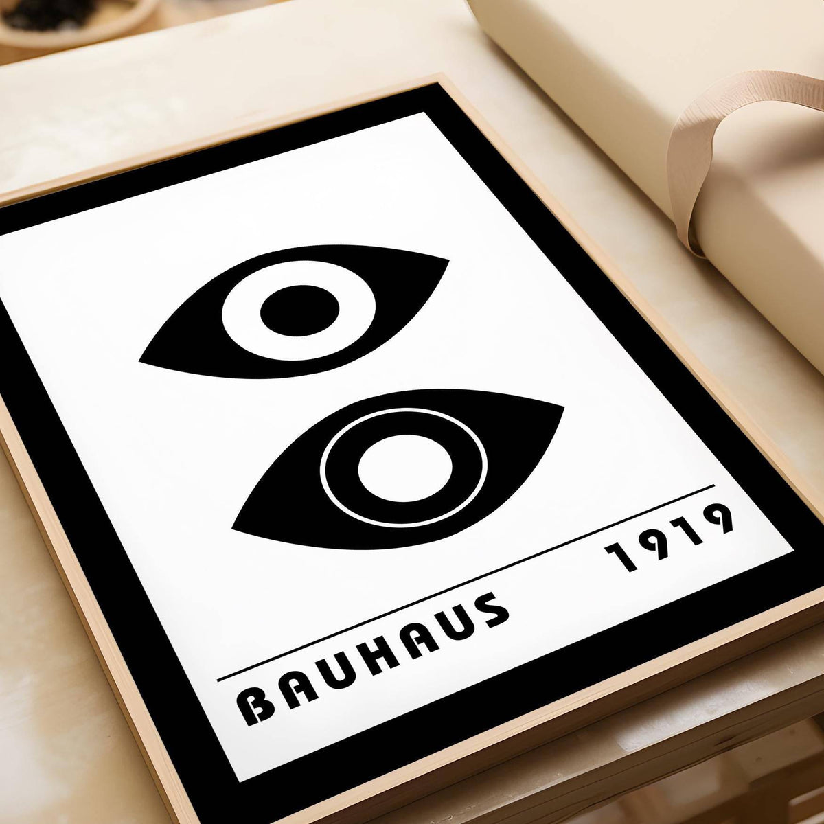 Framed Bauhaus Art Print with stylised eyes and black and white minimalist design leaning on a cream surface next to wrapping paper