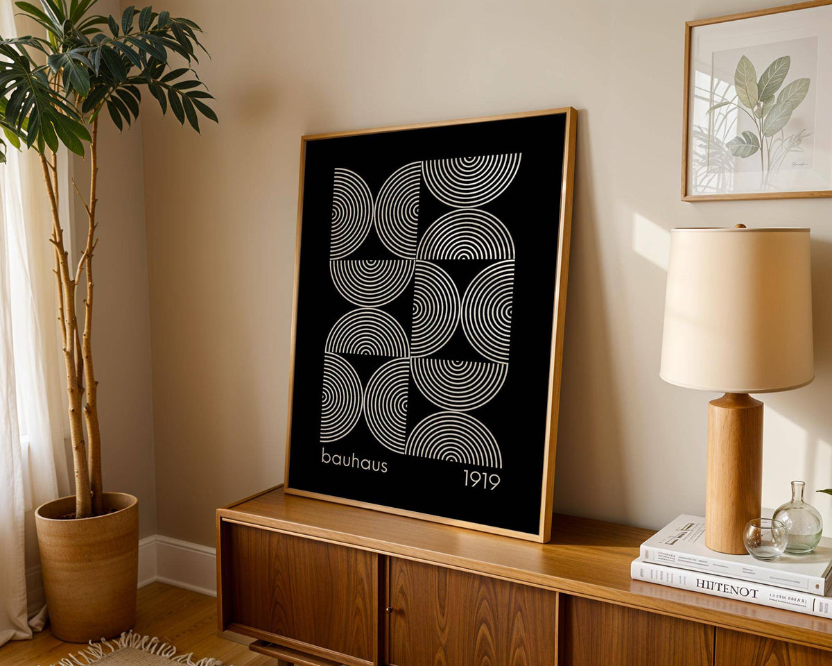 Geometric wall art with concentric circle pattern in black and white leaning on a wooden sideboard with lamp