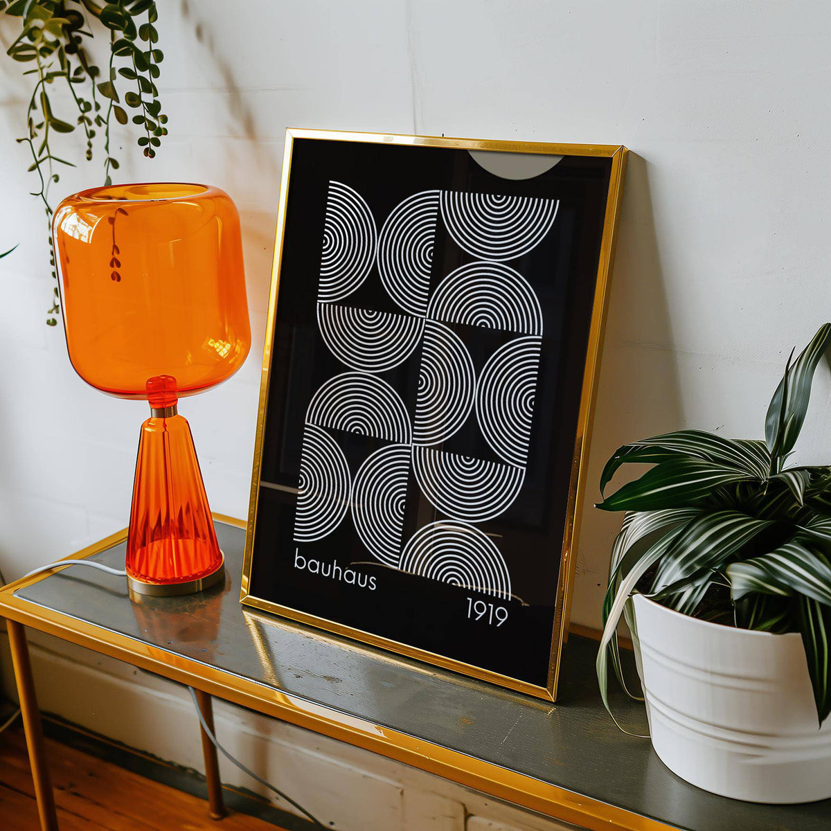 Framed Geometric wall art with white concentric circle pattern on black background beside orange lamp and green plant
