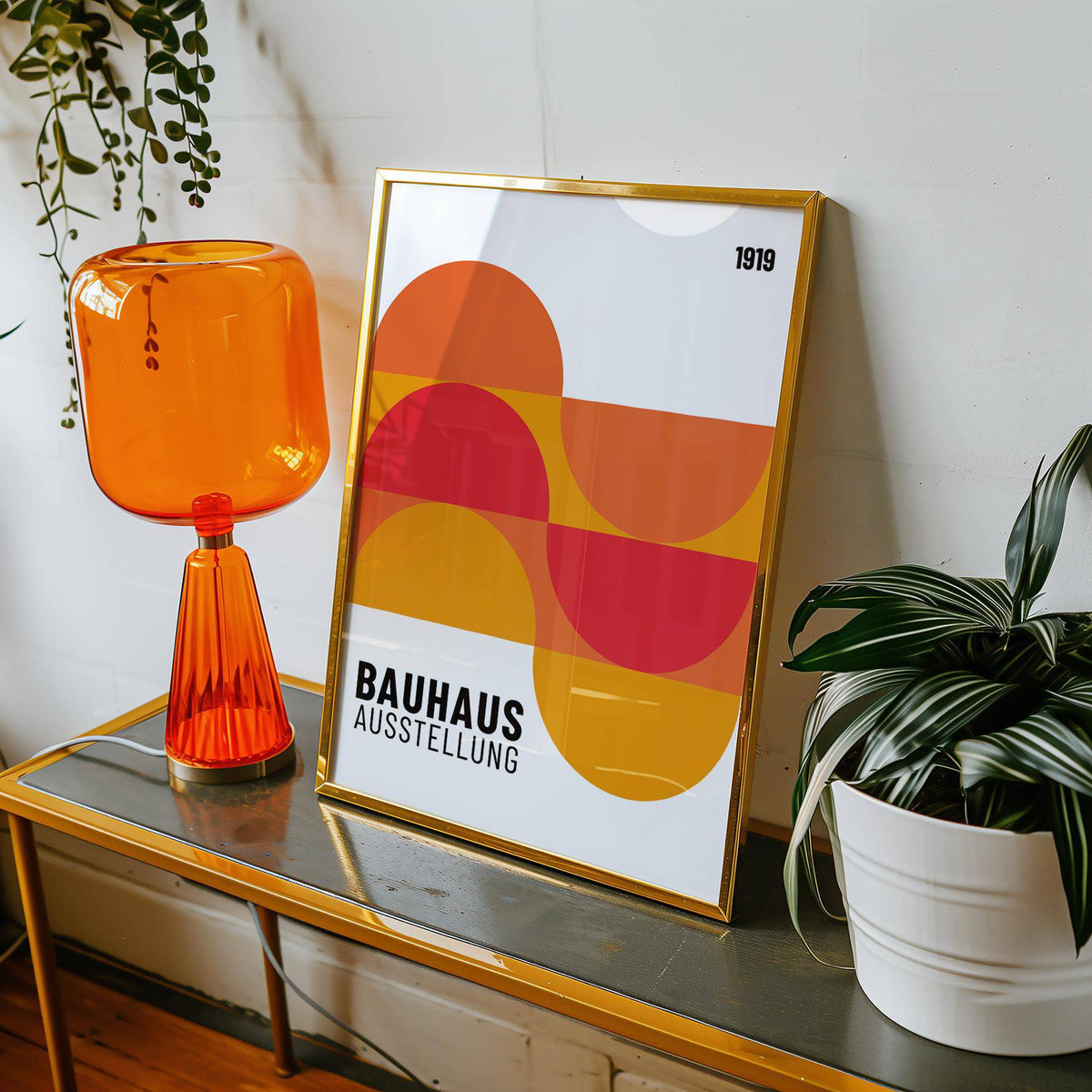 Framed Inexpensive Artwork with abstract geometric shapes in orange and red on a glass table with orange lamp and potted plant