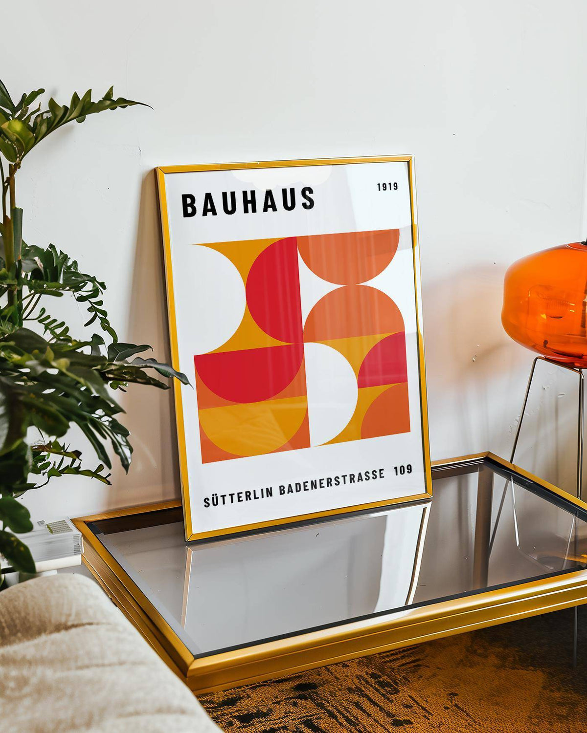 Mid Century wall art leaning on a glass coffee table with a yellow frame and geometric shapes in red and orange