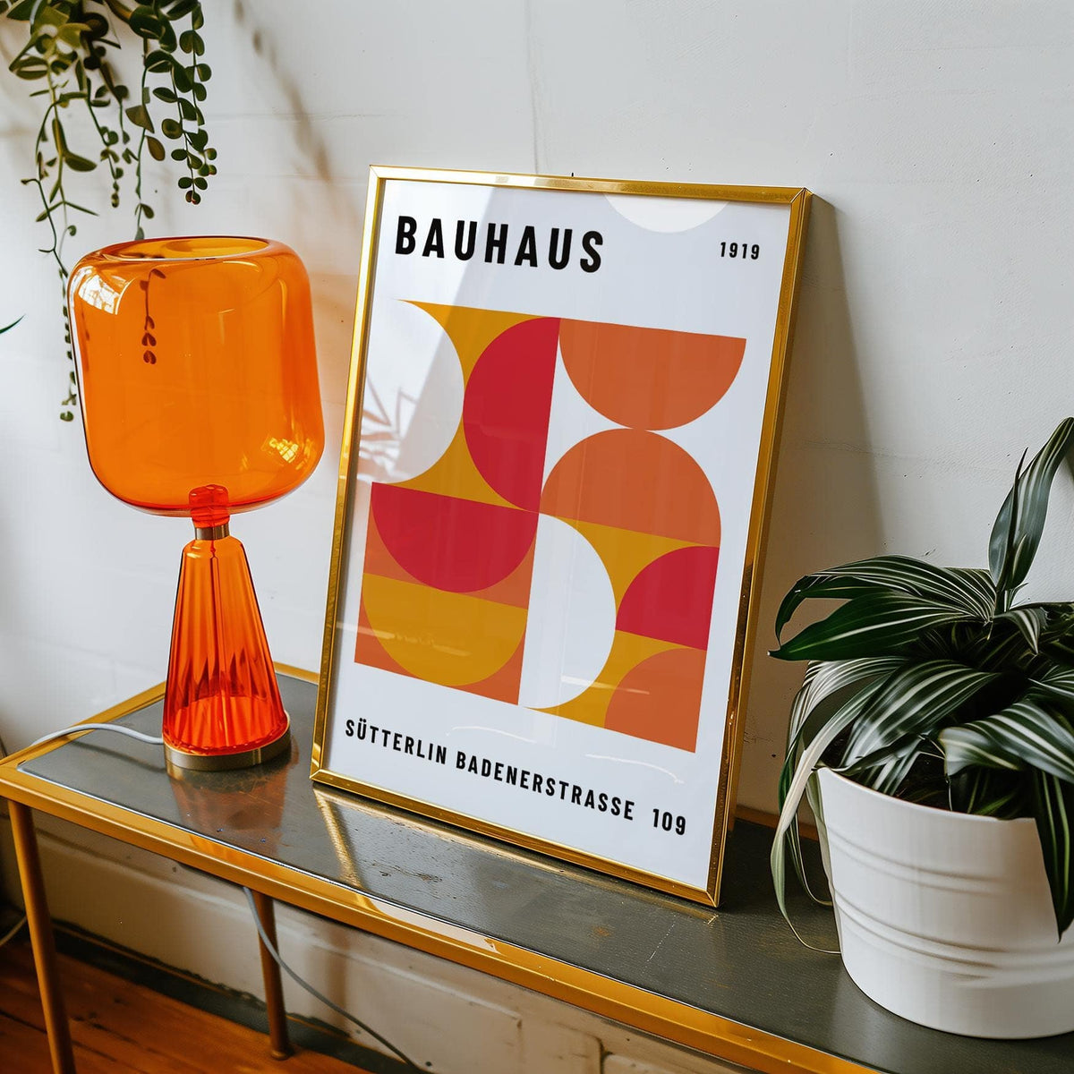Mid Century wall art framed close-up with orange and red geometric shapes and text leaning on a table with an orange lamp