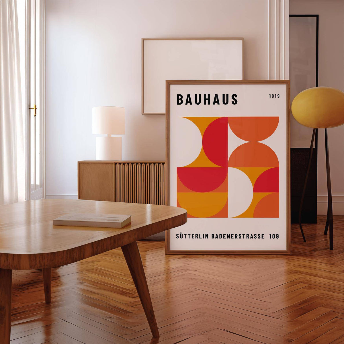 Mid Century wall art with geometric shapes in red and orange leaning on a wooden floor near a lamp