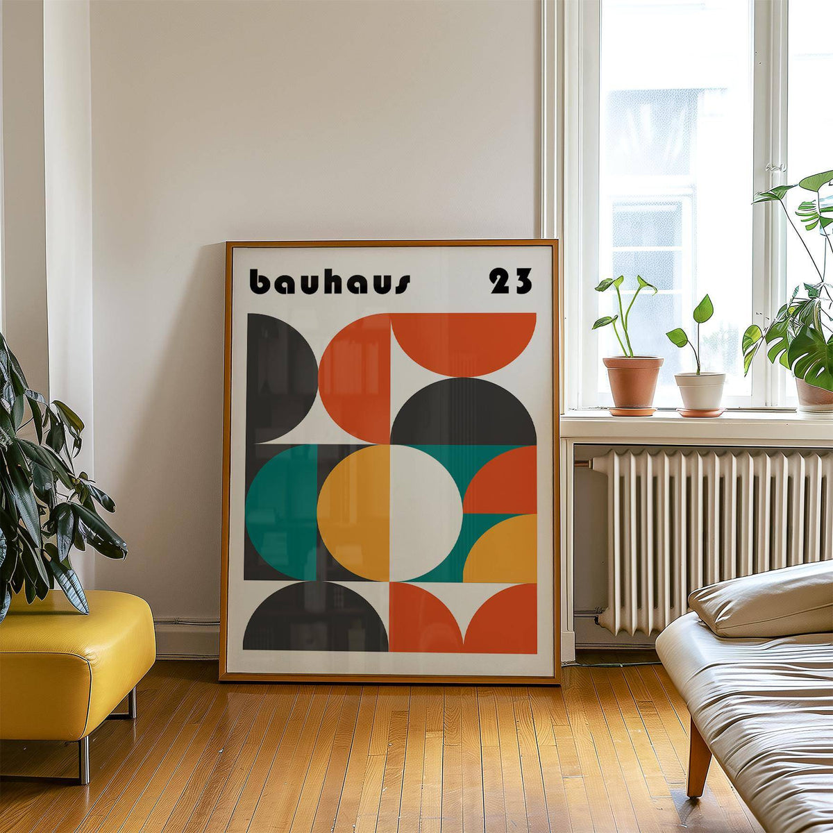 Print leaning on a wooden floor with geometric shapes in orange teal yellow and black beside a yellow ottoman with plants nearby