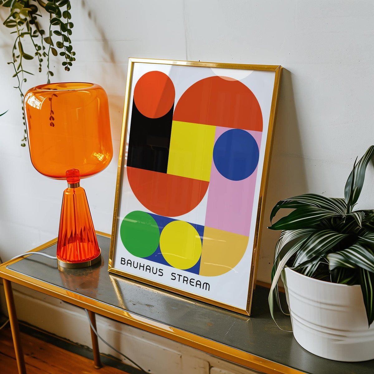 Framed Geometric Wall Decal with bright circles and rectangles in a gold frame on a table with an orange lamp and a plant