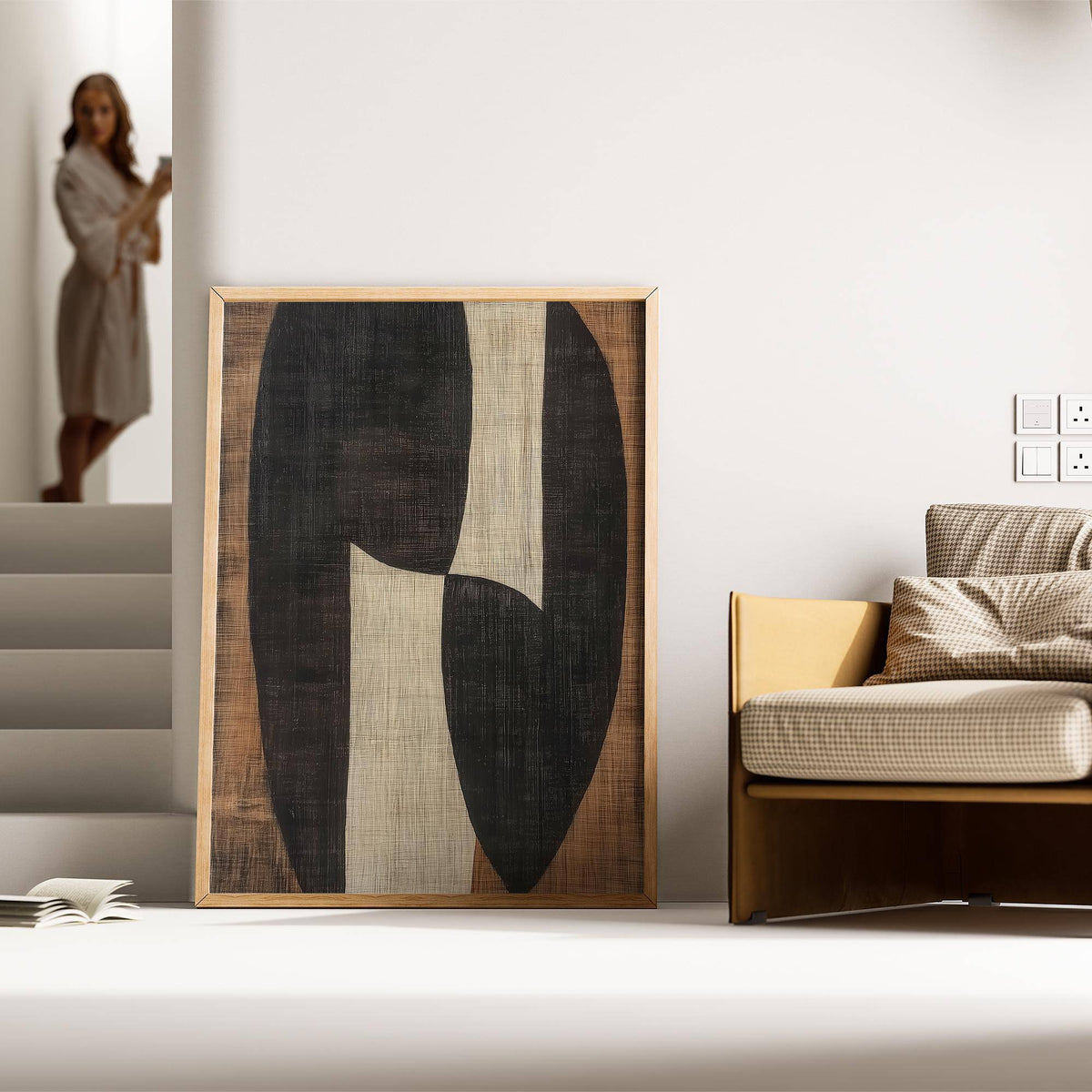 Zen wall art with abstract organic black and beige shapes leaning on the floor beside a beige sofa