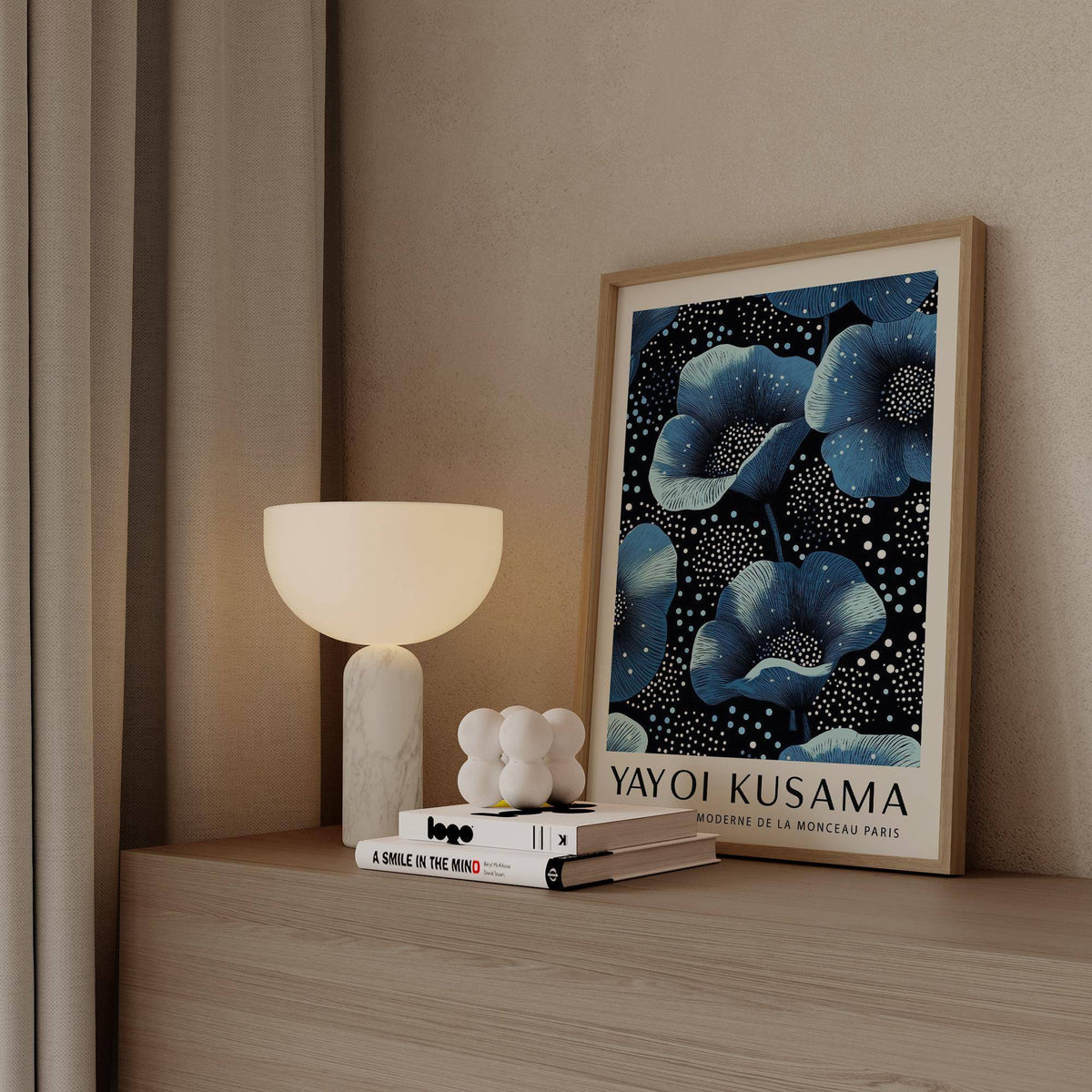 Framed print of blue flowers with white dots leaning on a wooden surface beside a lamp and books