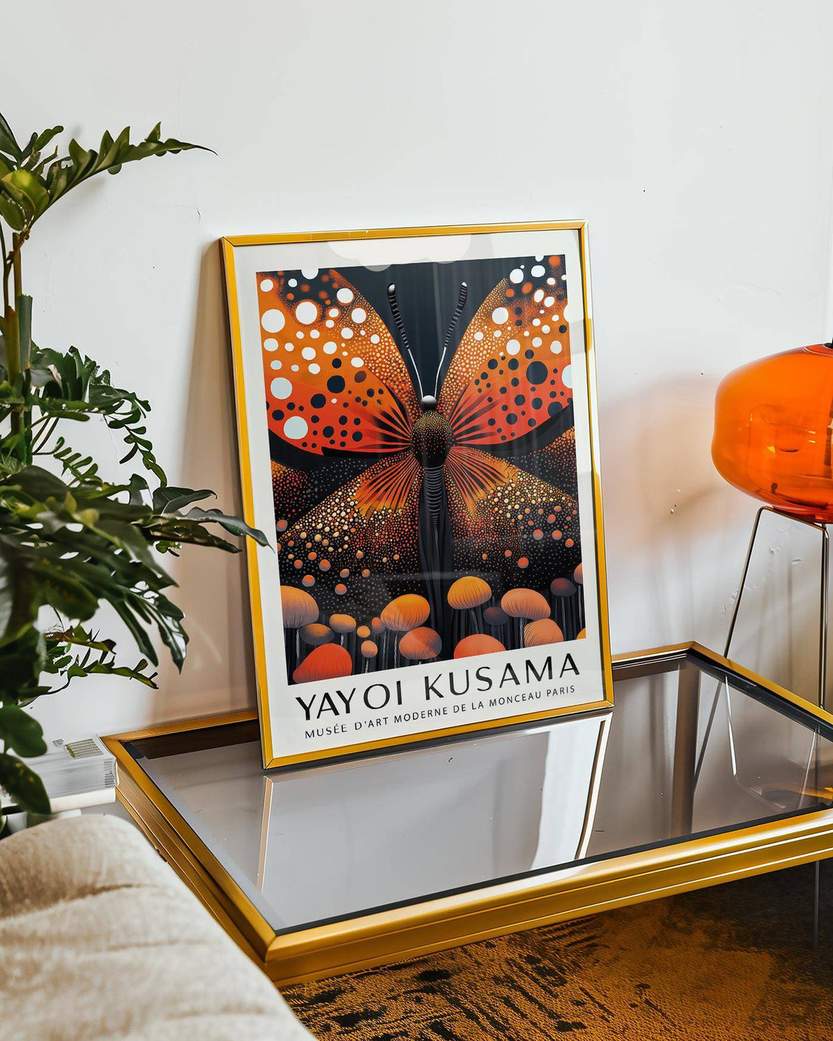 Abstract Butterfly Art framed print with orange butterfly and dotted detail leaning on a glass and gold coffee table near a plant