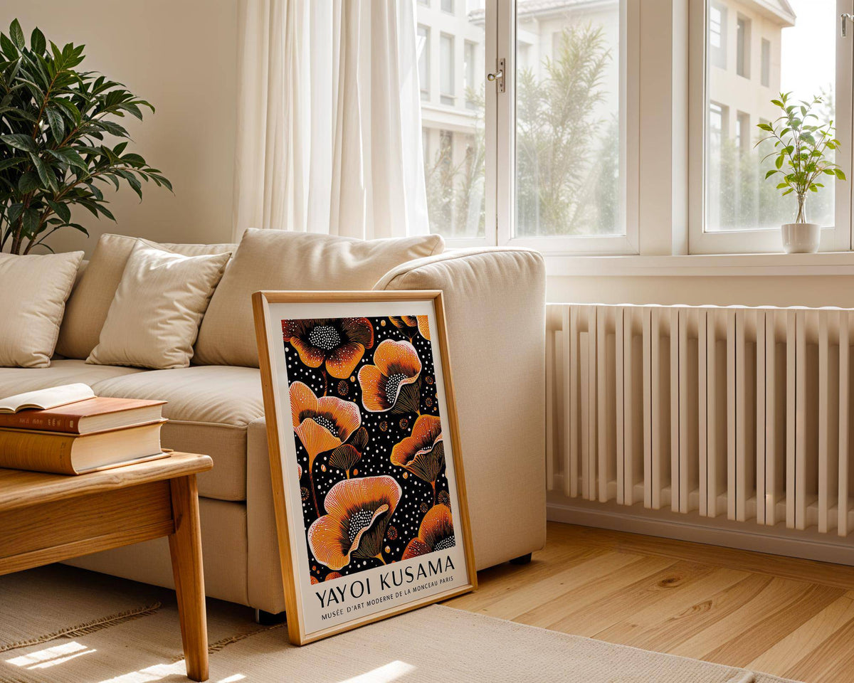 Orange print leaning on a wooden floor beside a white sofa and plant in a bright living room