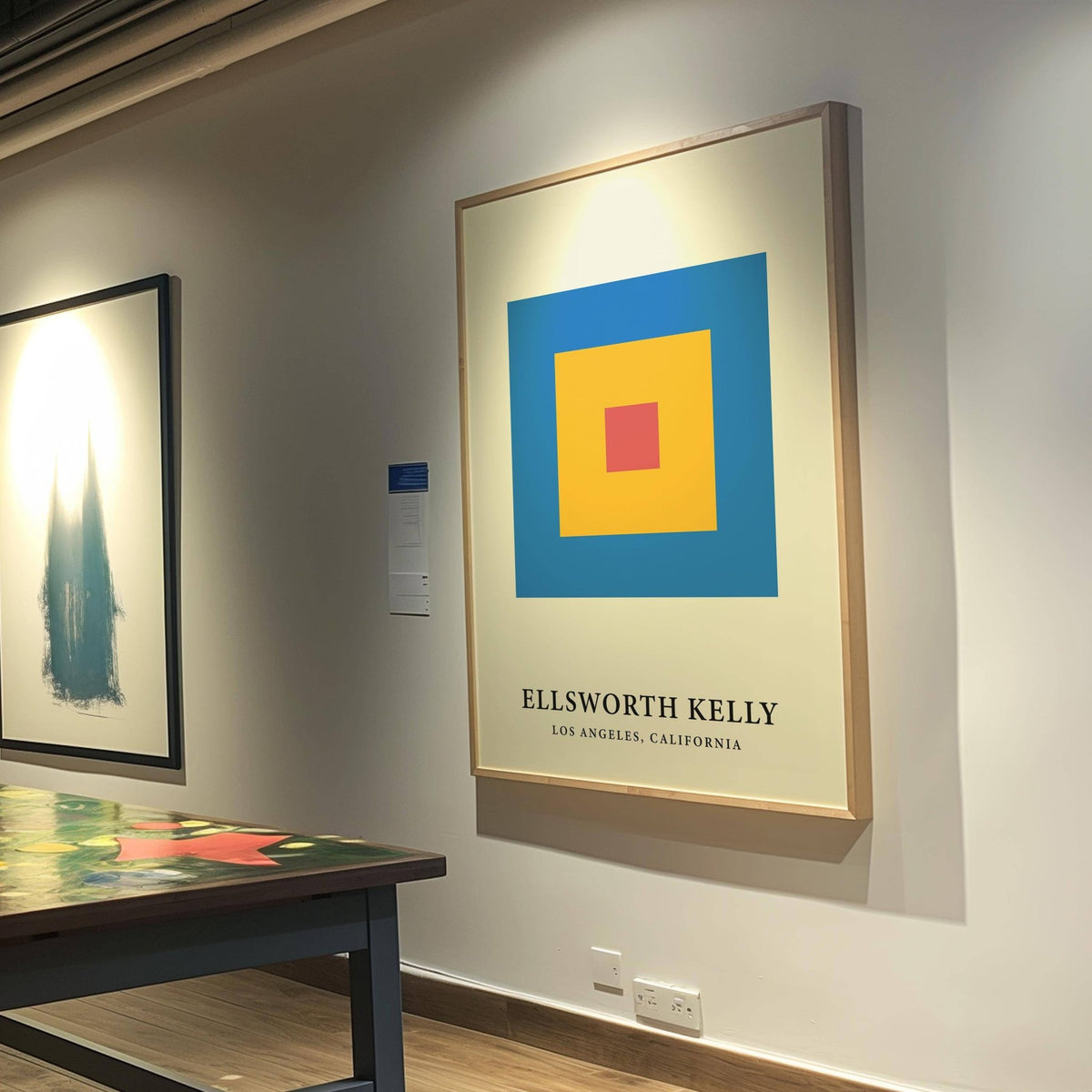 Minimalist Art framed print of concentric colour blocks in blue yellow and red on a gallery wall near a table