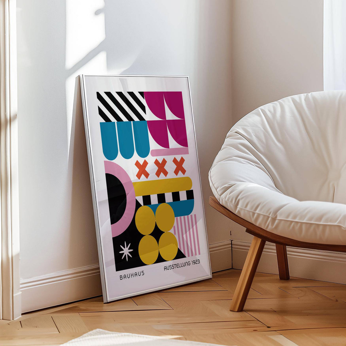 Print leaning on a floor of colorful geometric shapes in bauhaus style near a white cushioned chair