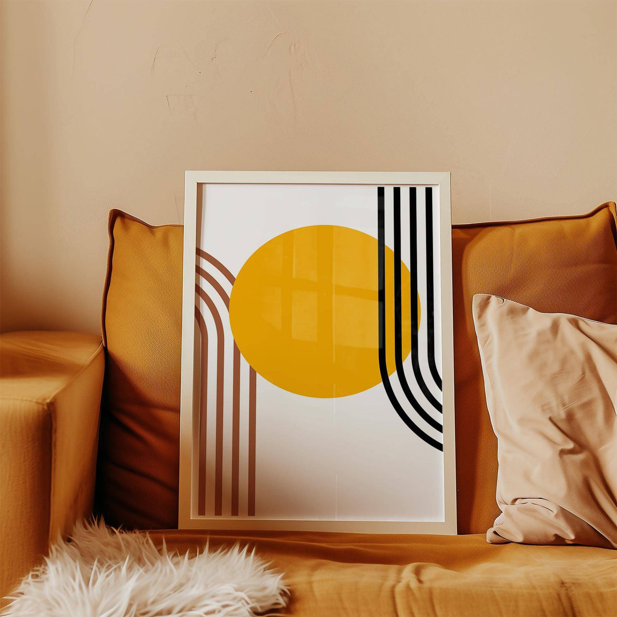 Bauhaus Sun print with orange circle and abstract stripes leaning on a mustard sofa with cushions