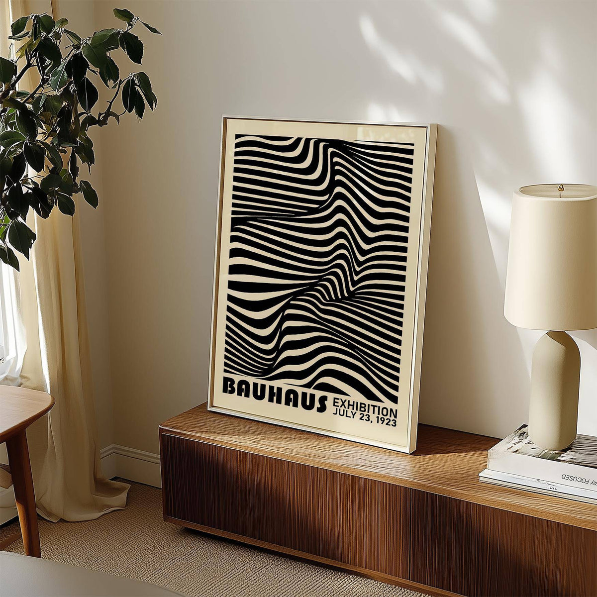 Black minimalist wall art leaning on a wooden sideboard next to a cream lamp and plant