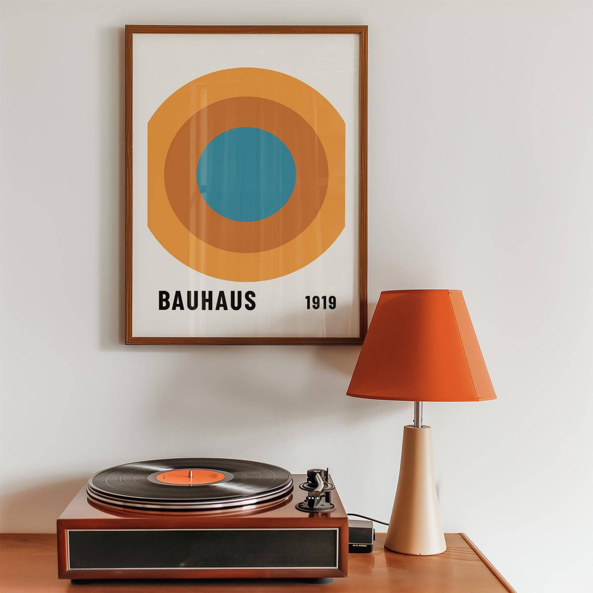 Bauhaus Circle Poster in a wooden frame with concentric circles in orange and blue above a wooden table with an orange lamp and record