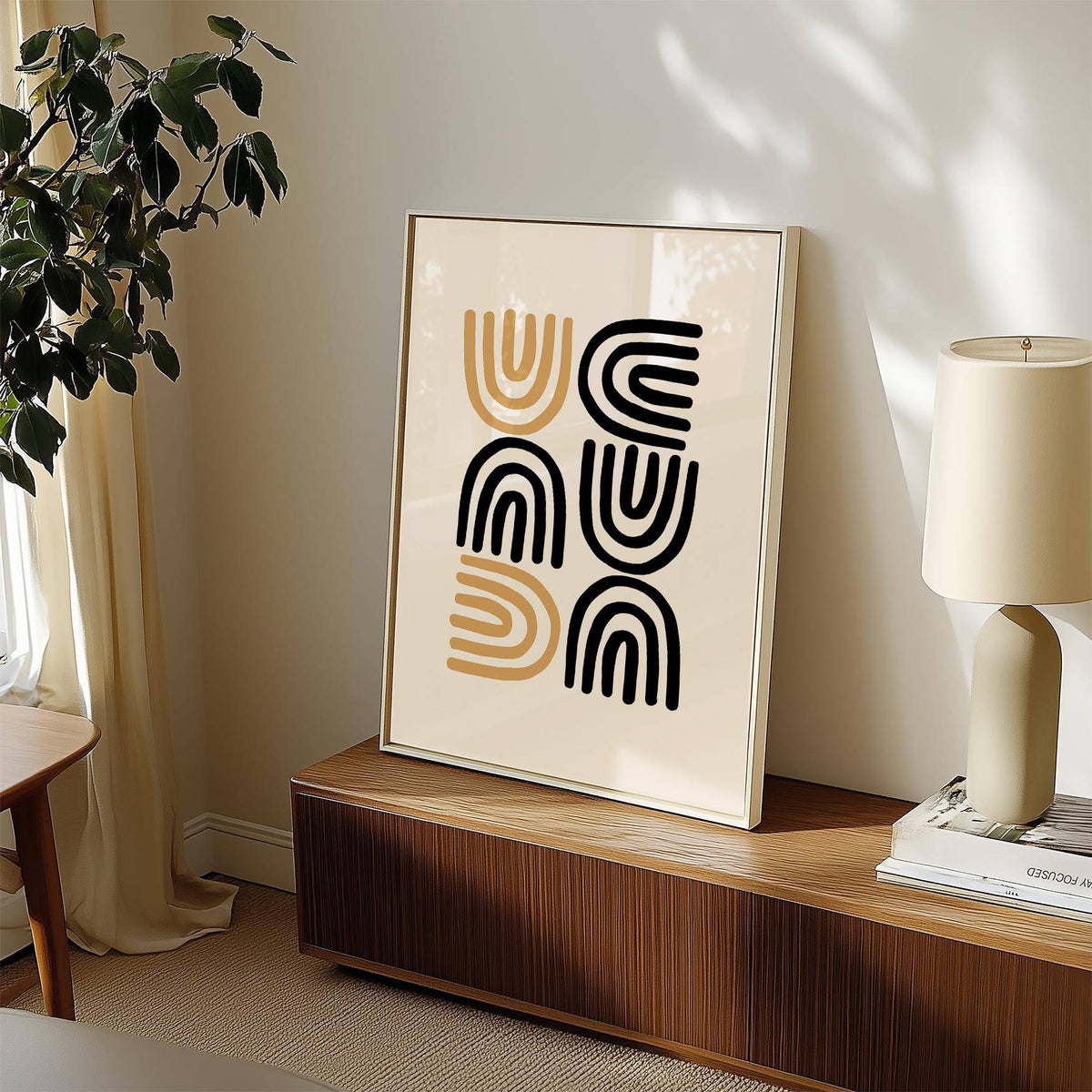 Black and Gold Pictures print with abstract black and gold arches leaning on a wooden sideboard with a lamp and plant nearby