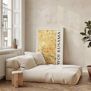 Print leaning on a floor next to a cream sofa with cushions and a potted plant against a beige wall