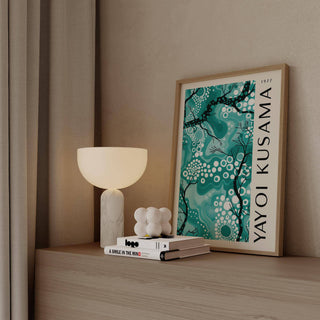 Teal wall decor with abstract branches and dots leaning on a wooden surface beside a lamp
