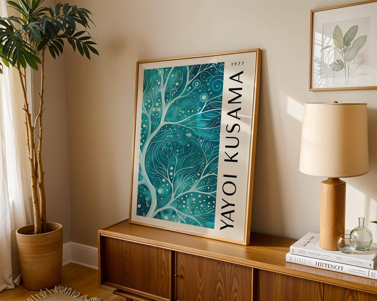 Teal color wall art with abstract teal branches leaning on a wooden sideboard beside a lamp and plant