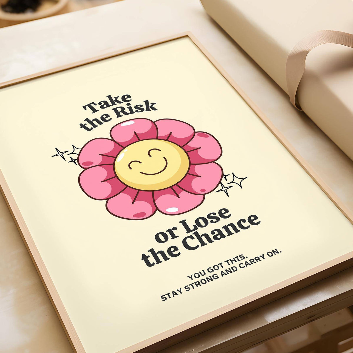 Framed Motivational Quotes wall art with a smiling pink flower and beige background leaning on a table