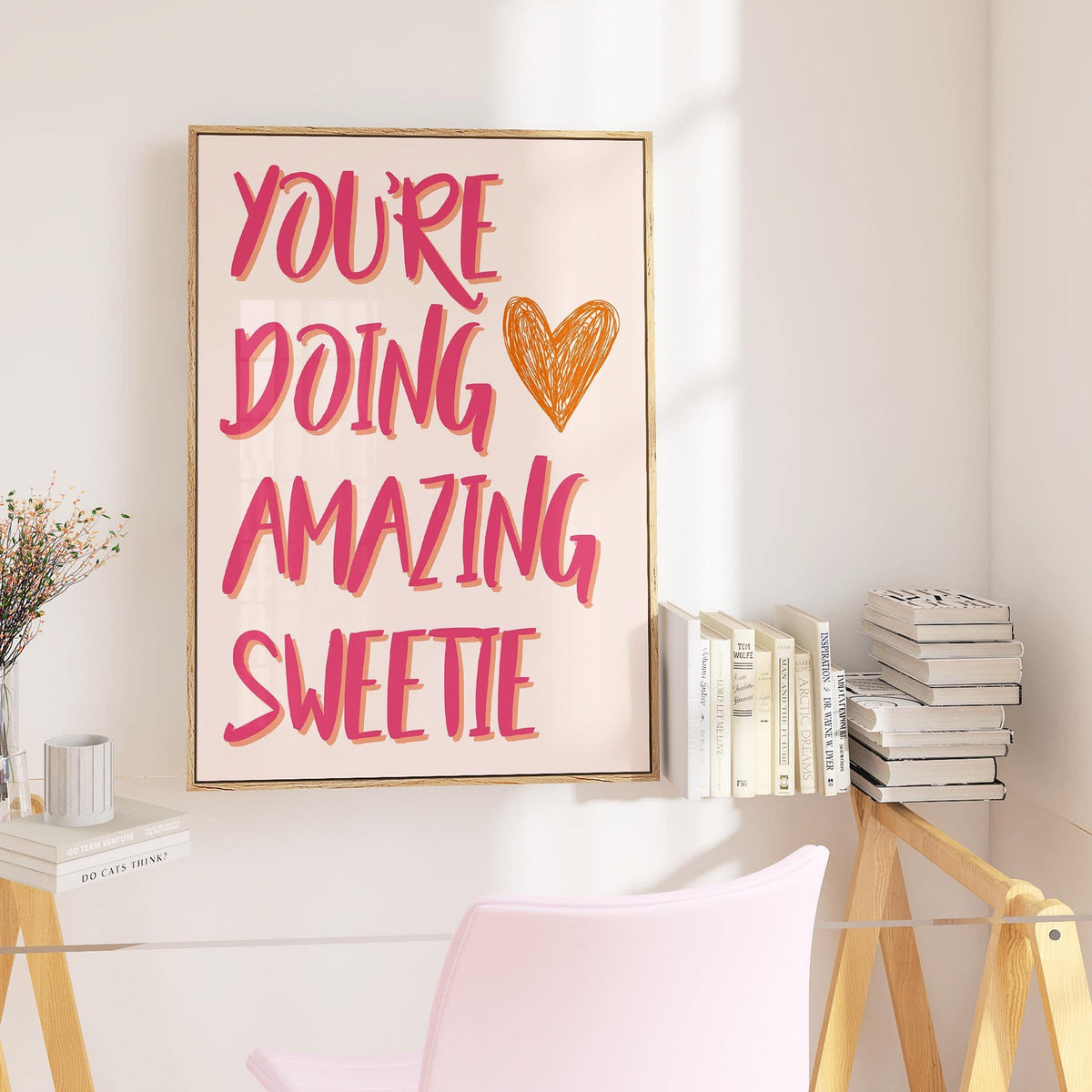 Good Motivational Posters framed print with pink and orange text above a glass desk with books and a pink chair