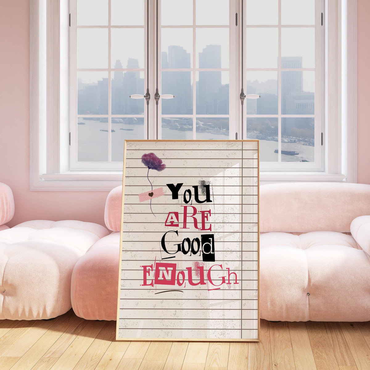 Posters of Positivity print leaning on a wooden floor with a pink couch and windows behind
